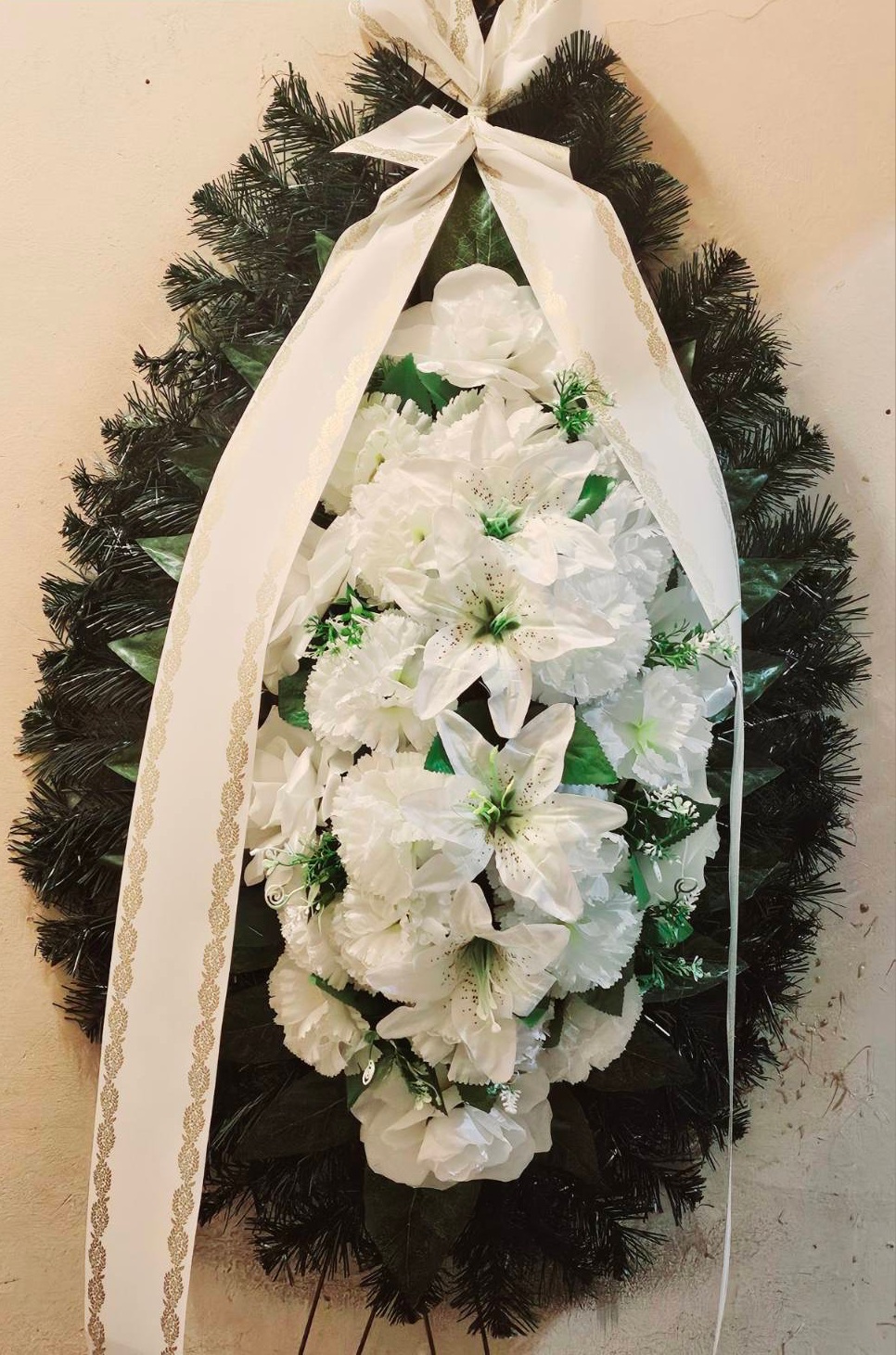 Траурен венец с бели лилии, рози и зеленина, украсен с бяла панделка