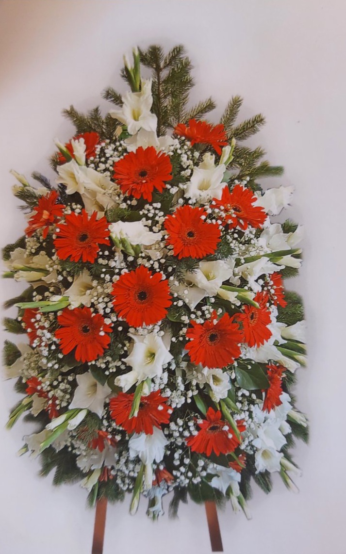Траурен венец с червени гербери, бели гладиоли и зеленина, поставен на стойка